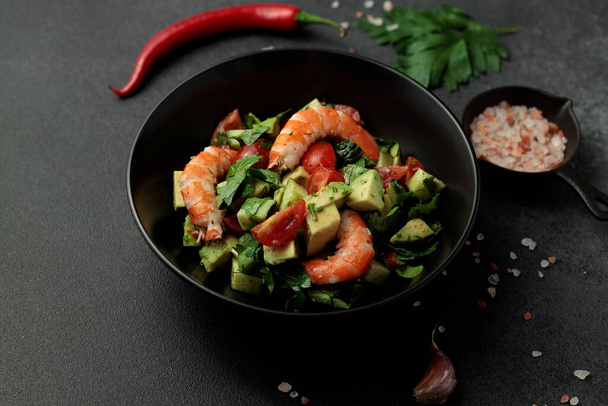 Salat aus Riesengarnelen, Avocado, Gurken, Tomaten und Kräutern. Schwarzer Hintergrund - Foto, Bild