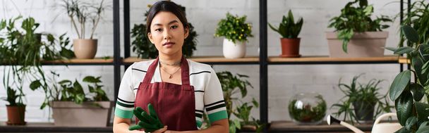 Młoda Azjatka, właścicielka małego zakładu, stoi pewnie w swoim sklepie, otoczona bujną zielenią. - Zdjęcie, obraz