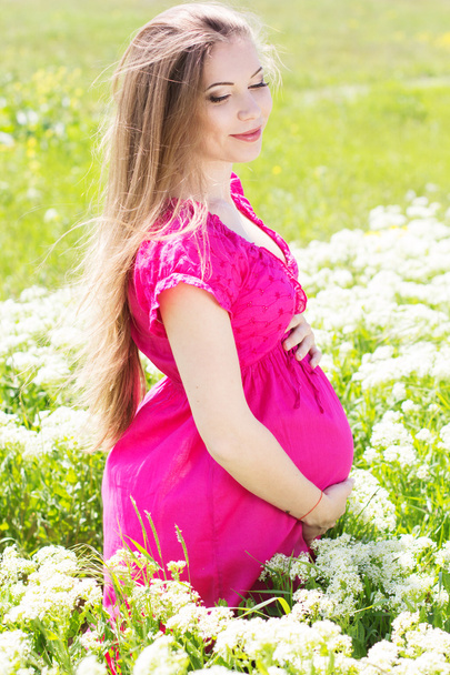 Happy pregnant woman sitting in green field - Zdjęcie, obraz