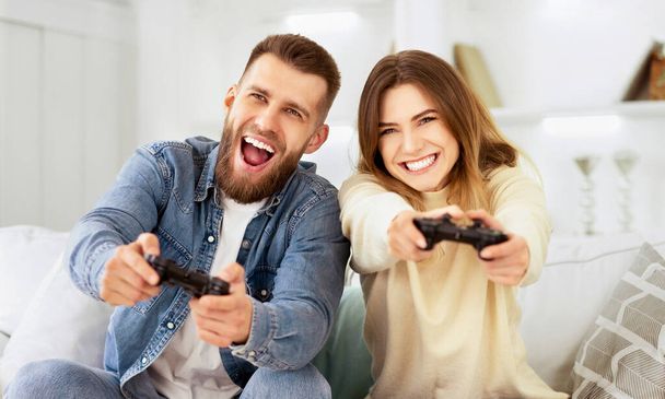 Naurava pari pelaa videopelejä joysticks, lepää sohvalla
 - Valokuva, kuva