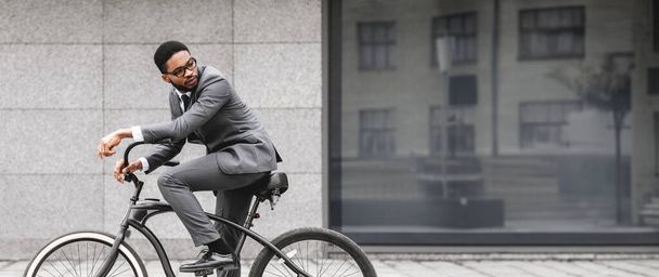 Afroamerikkalainen liikemies pyöränsä kanssa seisoo harmaalla muurilla kaupungissa. Asetelma on moderni ja kaupunkien, esittelee tyylikäs ja aktiivinen työmatka. - Valokuva, kuva