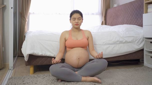 Портрет счастливой азиатской беременной женщины в спальне дома. Завести ребенка. Тренировка. Упражнения внутри помещений со спортивным оборудованием. Атлетично. Семейный образ жизни. Мама любит. Отдых. - Фото, изображение