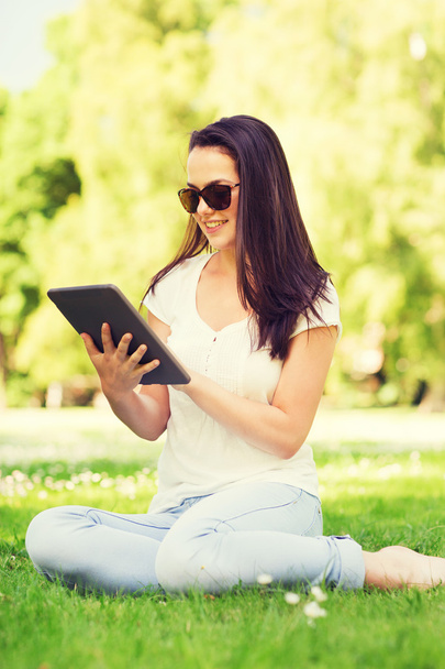 smiling young girl with tablet pc sitting on grass - Foto, Imagen