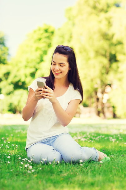 hymyilevä nuori tyttö älypuhelin istuu puistossa
 - Valokuva, kuva