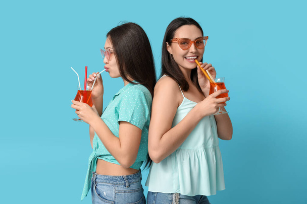 Beautiful young women with glasses of cocktail on blue background. Summer party - Фото, зображення