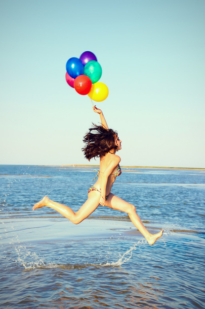Beautiful and athletic brunette girl with colorful balloons jump - Photo, Image