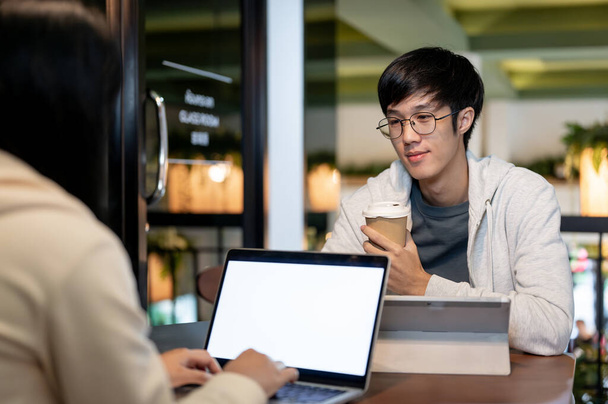Egy fiatal ázsiai férfi főiskolai hallgató találkozik a barátjával egy könyvtárban vagy kávézóban, hogy együtt dolgozzanak egy projekten. emberek és oktatási koncepciók - Fotó, kép