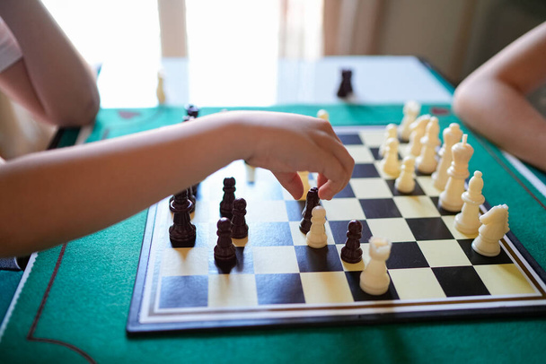 Dvě děti hrají šachovou partii. Jedno z dětí se natahuje pro kousek. Hra se hraje na zelené desce - Fotografie, Obrázek