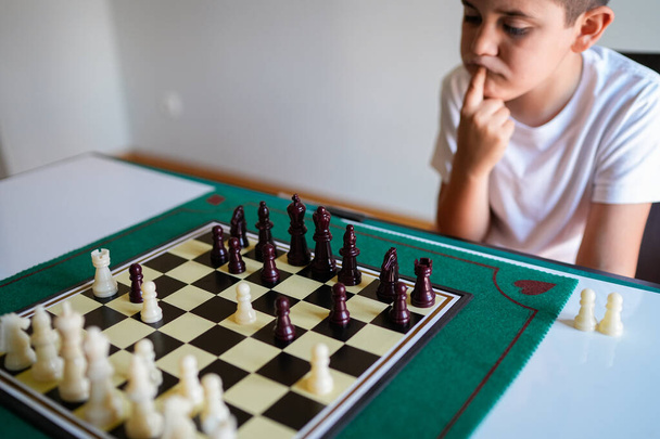 Chlapec hraje šachy a přemýšlí o svém dalším tahu. Hra je na zelené desce s černými a bílými čtverci - Fotografie, Obrázek