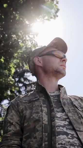 El joven soldado mira hacia el lado izquierdo del marco. Disparo estabilizado. Luz solar de día, destello de lente, retroiluminación. Texto en el pecho significa "Fuerzas de Asalto Aéreo Ucranianas" y "Fuerzas Armadas de Ucrania". Vídeo vertical - Metraje, vídeo