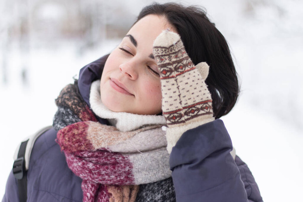 Молода усміхнена красива жінка в шарфі на відкритому повітрі під час снігопаду - Фото, зображення