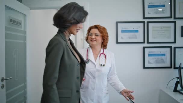 Médecin souriant accueillant le patient dans le gros plan du cabinet médical. Médecin professionnel positif en manteau blanc saluant femme brune à la clinique moderne. Dame chic va sur rendez-vous de soins de santé à l'hôpital. - Séquence, vidéo
