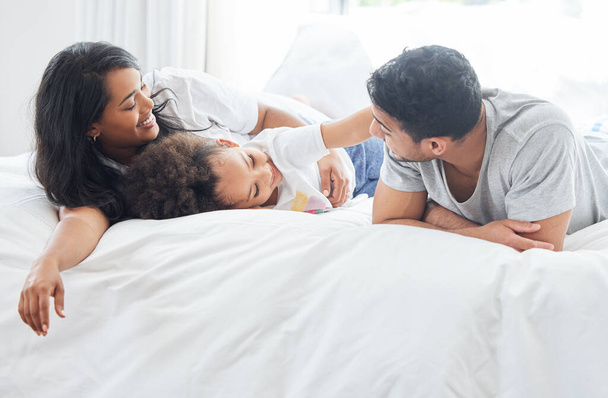 Child, parents and family in bed for morning with love relationship, parent support and bonding together in home. Mother, father and young girl in bedroom for wake up with lazy weekend and relax. - Photo, Image
