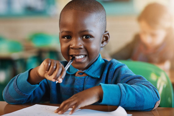 École primaire, salle de classe et portrait de l'enfant avec papier pour l'éducation, l'apprentissage et l'évaluation. Joyeux, visage et noir garçon par bureau avec stylo pour le développement de l'enfant, la leçon et la croissance des connaissances. - Photo, image