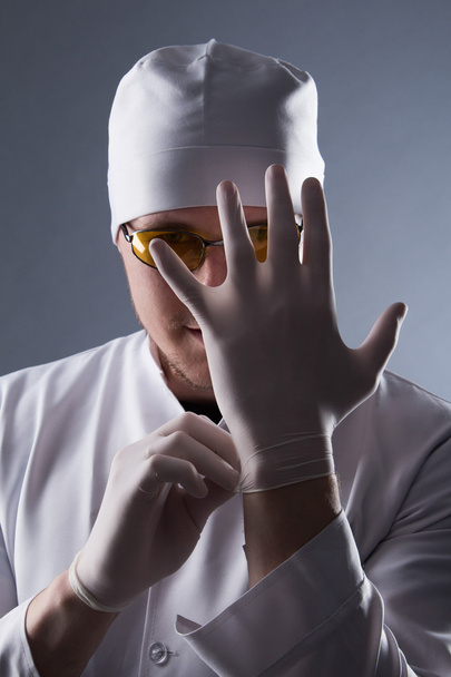 Médico masculino em boné e óculos usar luvas de borracha médica em con
 - Foto, Imagem
