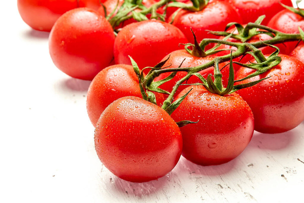 Un manojo de tomates cherry maduros con gotas de agua en la superficie de madera blanca. Primer plano de tomates cherry. Orientación vertical de la foto - Foto, imagen