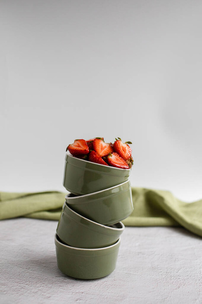 A few small bowls stand on top of each other. Strawberries lie on top in a bowl, green canvas behind - Photo, Image