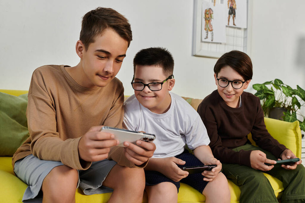 Three boys sit on a yellow couch, playing games on their phones. - Photo, Image