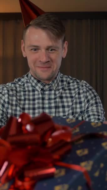 POV Attrayant mâle obtenir boîte cadeau d'anniversaire avec grand arc rouge dans le salon de la maison confortable et heureux de l'attention à lui plan vertical. - Séquence, vidéo