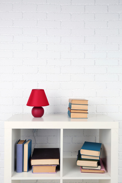 Wooden shelf with books and lamp on brick wall background - Photo, Image