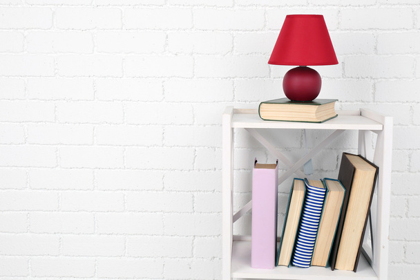 Wooden shelf with books and lamp on brick wall background - Zdjęcie, obraz