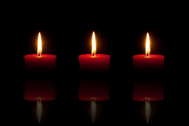 Три палаючі червоні свічки перед чорним тлом
 - Фото, зображення