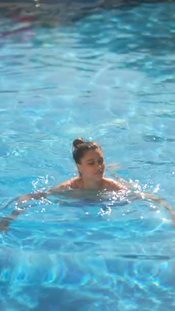 Kobieta ciesząca się kąpielą w jasnoniebieskim basenie w pogodny, słoneczny dzień. Idealny na letnie i wakacyjne tematy. - Materiał filmowy, wideo