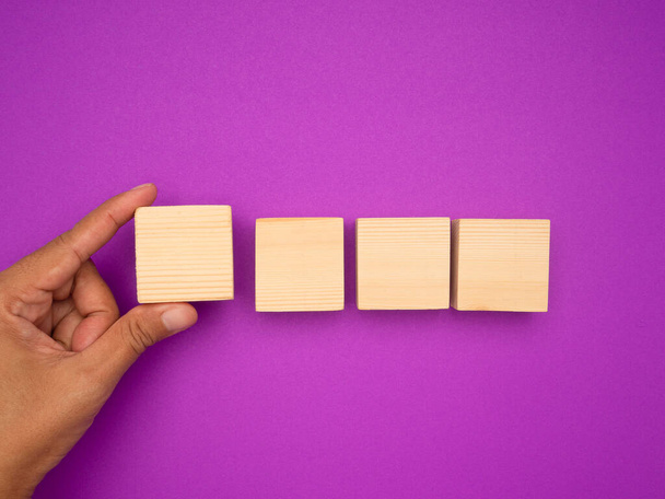 Vista aerea di mano che tiene un cubo di legno bianco e tre disposti in fila su uno sfondo viola. Spazio per testo - Foto, immagini