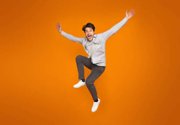 Divertente uomo che salta con le braccia sollevate su sfondo arancione studio
 - Foto, immagini