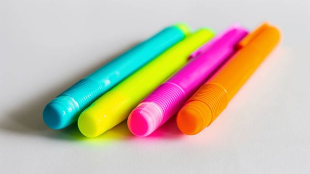 Cztery kolorowe długopisy w kolorze niebieskim, żółtym, różowym i pomarańczowym, umieszczone obok siebie na białym tle. - Zdjęcie, obraz