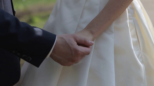 Gently connected hands of a newly-married couple with wedding rings on a finger on a background of a white wedding dress - 映像、動画