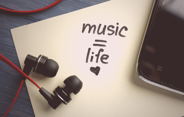 Earphones with text Music - life on sticker on wooden table, closeup - Fotó, kép