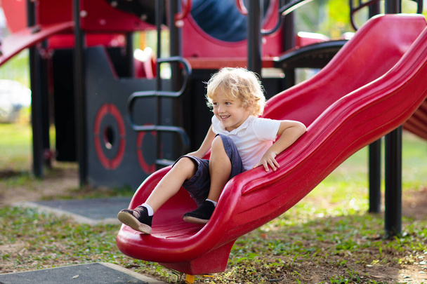 Child playing on outdoor playground. Kids play on school or kindergarten yard. Active kid on colorful slide and swing. Healthy summer activity for children. Little boy climbing outdoors. - Photo, Image