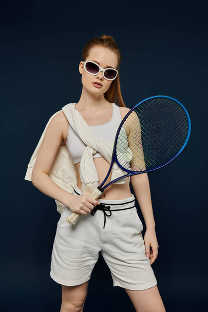 Güneş gözlüklü şık bir kadın canlı bir arkaplana karşı tenis raketi tutuyor.. - Fotoğraf, Görsel
