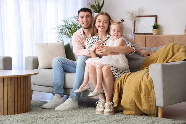 自宅でソファーで抱擁する彼らの小さな娘と幸せな両親 - 写真・画像