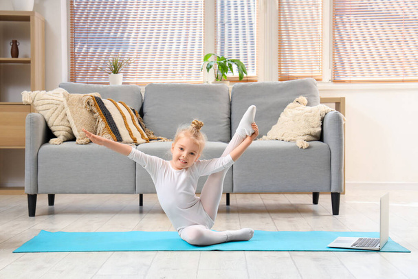 Cute little girl doing gymnastics with laptop at home - Zdjęcie, obraz