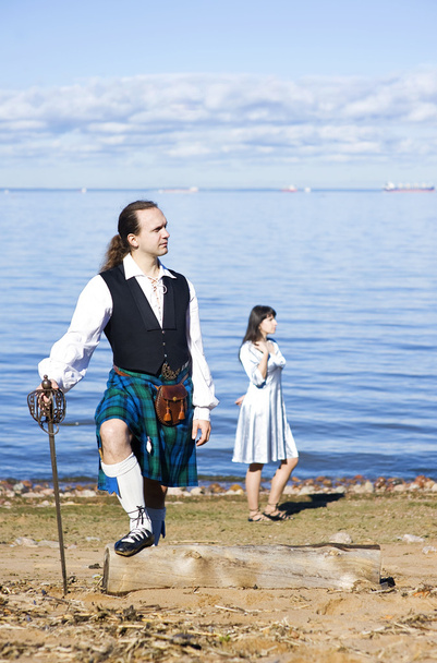 ο άνθρωπος στο κοστούμι Σκωτίας και γυναίκα κοντά στη θάλασσα - Φωτογραφία, εικόνα