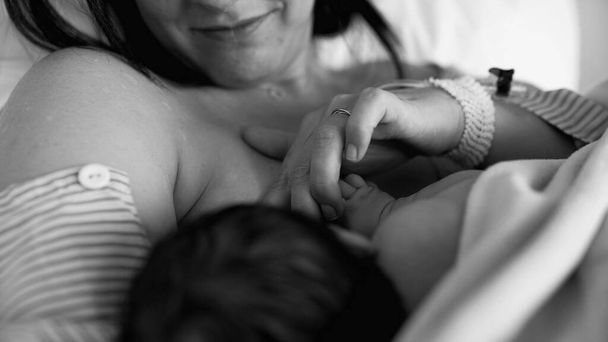 Monochroom moment van nieuwe moeder borstvoeding haar pasgeboren baby na de bevalling in zwart-wit in het ziekenhuis - Foto, afbeelding