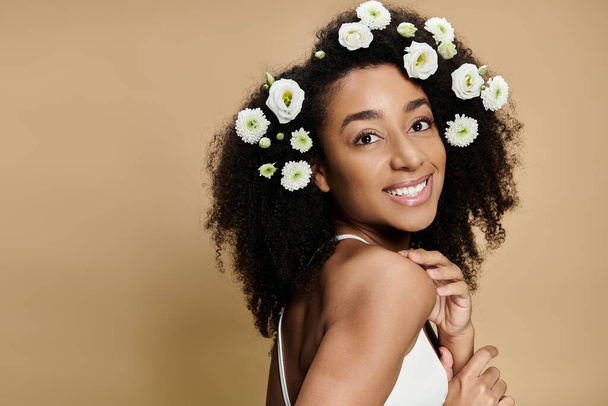 Uma bela mulher afro-americana com maquiagem natural e flores em seu cabelo sorri contra um fundo bege. - Foto, Imagem
