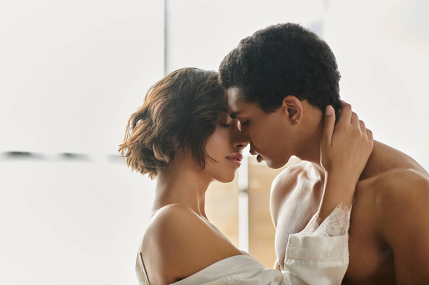 Una donna asiatica e un uomo afroamericano condividono un momento tenero, abbracciando e baciando appassionatamente su un letto. - Foto, immagini
