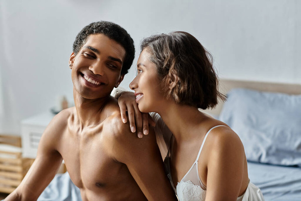 Mladá Asiatka a Afroameričan se tulí na posteli, usmívají se a dívají se na sebe s láskou. - Fotografie, Obrázek