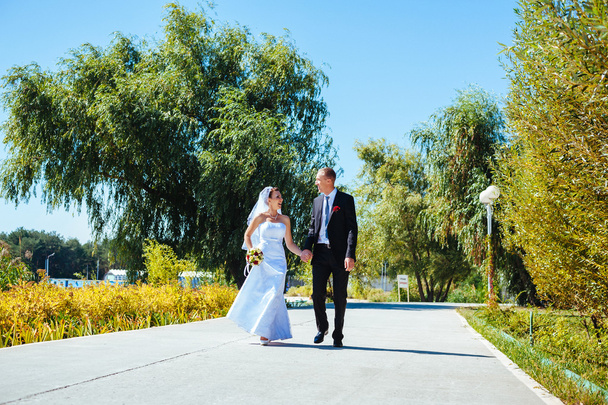νύφη και γαμπρός στο περπάτημα σε εξωτερικούς χώρους για την ημέρα του γάμου άνοιξη φύση. νυφικό ζευγάρι, γυναίκα ευτυχισμένη νεόνυμφο και άνθρωπος, αγκαλιάζοντας σε καταπράσινο πάρκο. αγαπώντας το γαμήλιο ζεύγος εξωτερική. - Φωτογραφία, εικόνα