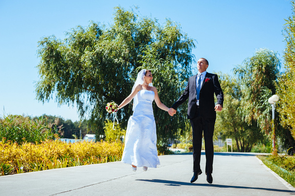 νύφη και γαμπρός στο περπάτημα σε εξωτερικούς χώρους για την ημέρα του γάμου άνοιξη φύση. νυφικό ζευγάρι, γυναίκα ευτυχισμένη νεόνυμφο και άνθρωπος, αγκαλιάζοντας σε καταπράσινο πάρκο. αγαπώντας το γαμήλιο ζεύγος εξωτερική. - Φωτογραφία, εικόνα