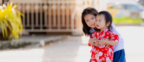 Portrait of Asian sibling embracing each other, in the evening after school, a younger brother comes to take his older sister home, A smiling elder sister in the city with her happy baby brother. - Photo, Image