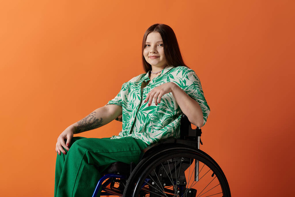 Una joven con el pelo castaño largo sonríe con confianza mientras está sentada en una silla de ruedas sobre un fondo naranja. - Foto, Imagen