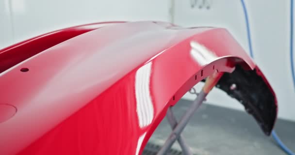 Primer plano de un parachoques de coche rojo que se pinta profesionalmente en un taller especializado de reparación de automóviles. Acabado brillante y liso. Fábrica de fabricación de automóviles. Servicios de pintura para automóviles, concepto de taller de carrocería - Metraje, vídeo