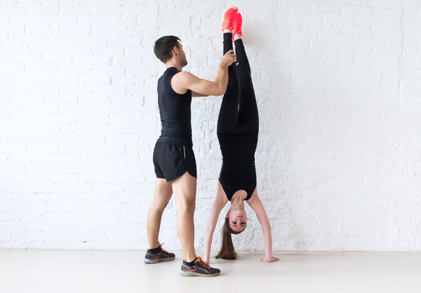 woman sportsman doing a handstand against concrete wall male trainer helping her concept sport, fitness, lifestyle and people - Photo, Image