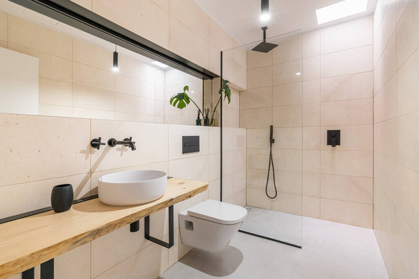 Φωτεινό κομψό ευρύχωρο μπάνιο με στρογγυλό νεροχύτη σε ξύλινο πάγκο, τουαλέτα και ντους. Η έννοια της νέας κατοικίας ή ανακαίνισης σε παλιό διαμέρισμα. - Φωτογραφία, εικόνα