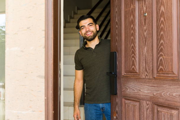 Homem hispânico acolher com um sorriso em sua porta da frente, criando uma atmosfera acolhedora para os hóspedes - Foto, Imagem