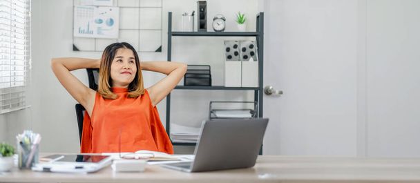 Eine Frau in orangefarbenem Hemd sitzt an einem Schreibtisch mit Laptop und Tablet. Sie ist entspannt und konzentriert auf ihre Arbeit - Foto, Bild